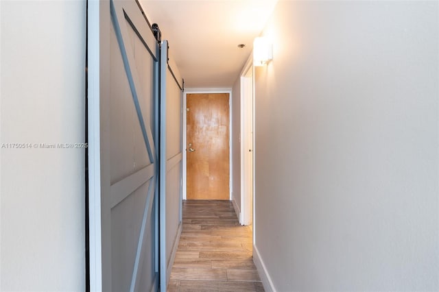 hall with light wood-type flooring, a barn door, and baseboards