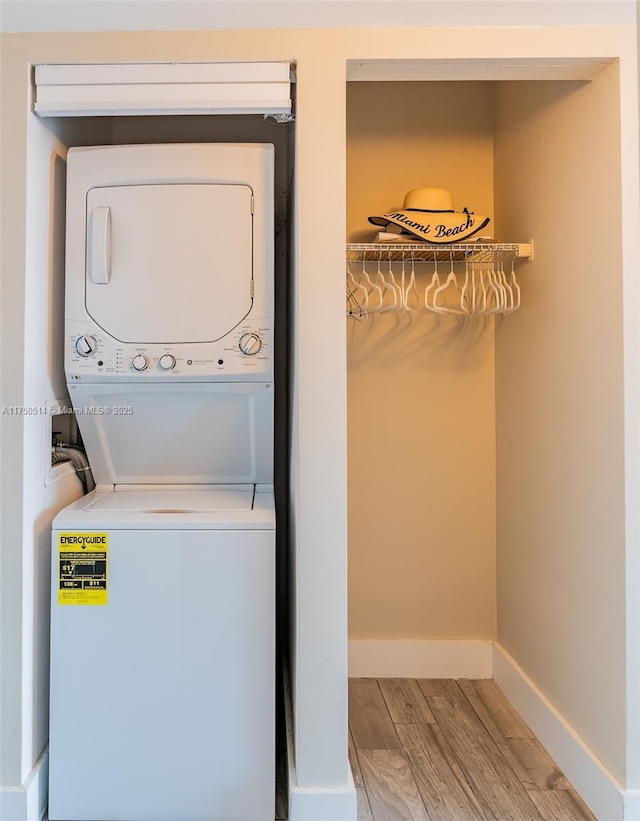 laundry area with laundry area, baseboards, stacked washer / drying machine, and wood finished floors