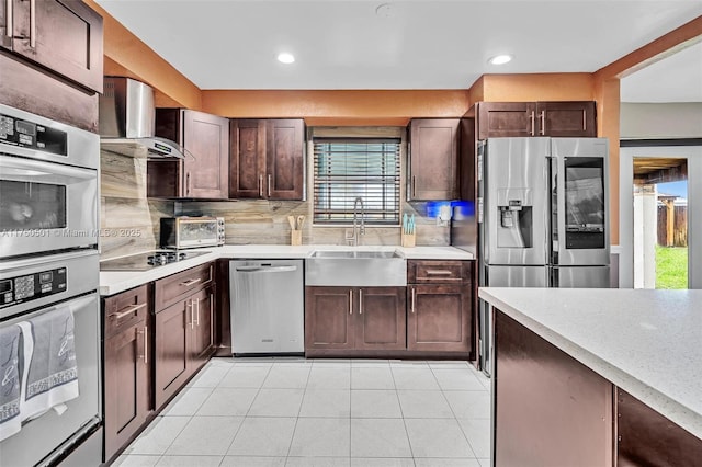 kitchen with appliances with stainless steel finishes, a sink, light countertops, wall chimney range hood, and backsplash