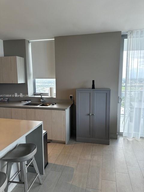 kitchen featuring a breakfast bar, gray cabinets, light countertops, light brown cabinetry, and a sink