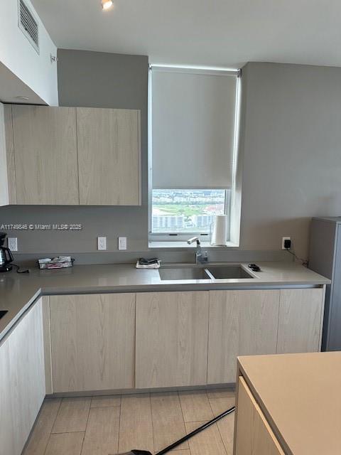 kitchen featuring light brown cabinets, visible vents, light countertops, and a sink