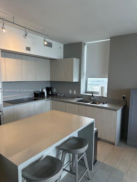 kitchen with black electric stovetop, a breakfast bar, a kitchen island, a sink, and visible vents