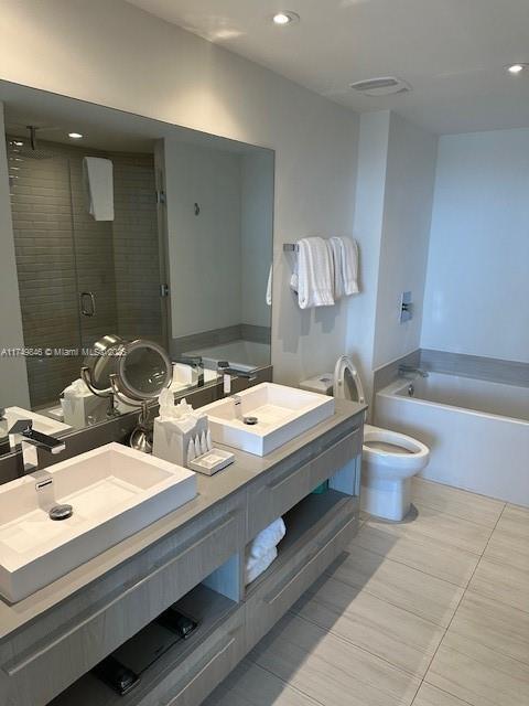 full bath with double vanity, a garden tub, a shower stall, and a sink