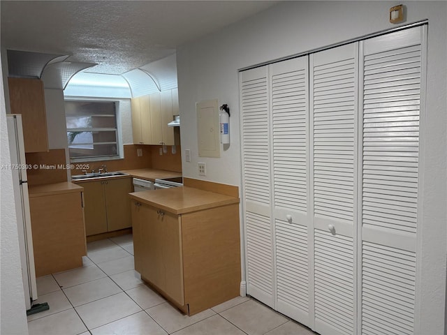 kitchen with light tile patterned flooring, under cabinet range hood, a peninsula, white appliances, and a sink