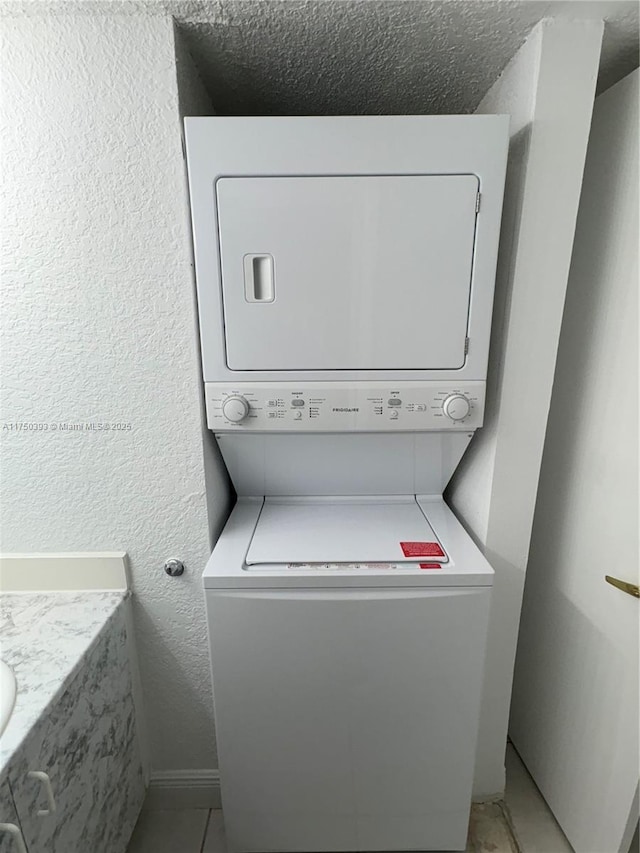 laundry room featuring a textured ceiling, a textured wall, laundry area, and stacked washer / drying machine