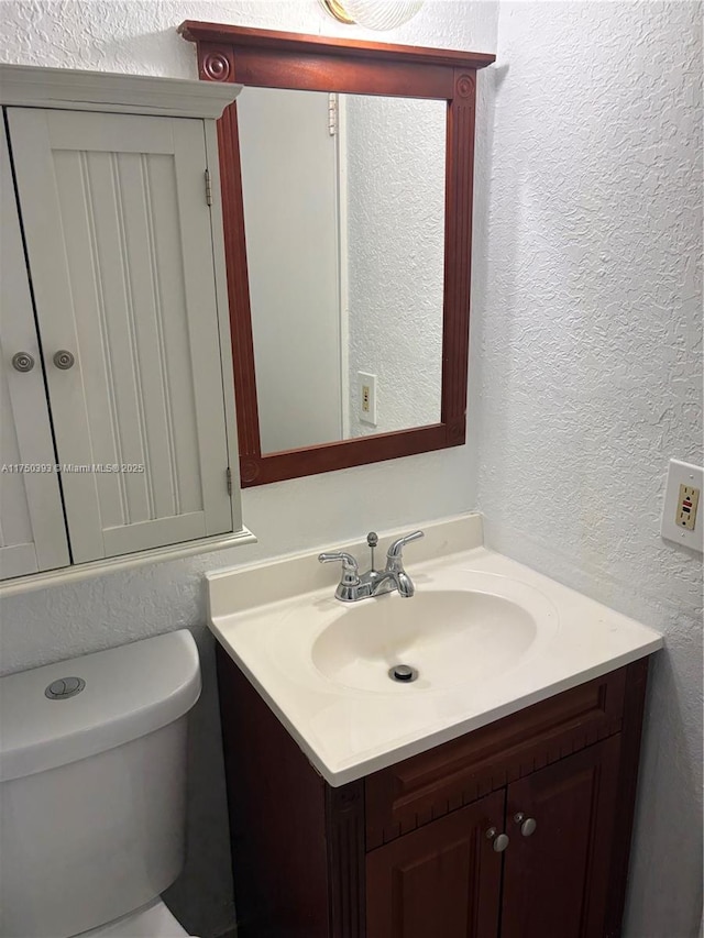 bathroom featuring a textured wall, vanity, and toilet