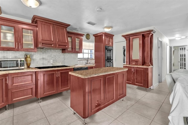 kitchen with a kitchen island, dark brown cabinets, light countertops, black appliances, and glass insert cabinets