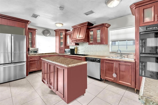 kitchen with a sink, visible vents, a kitchen island, black appliances, and glass insert cabinets