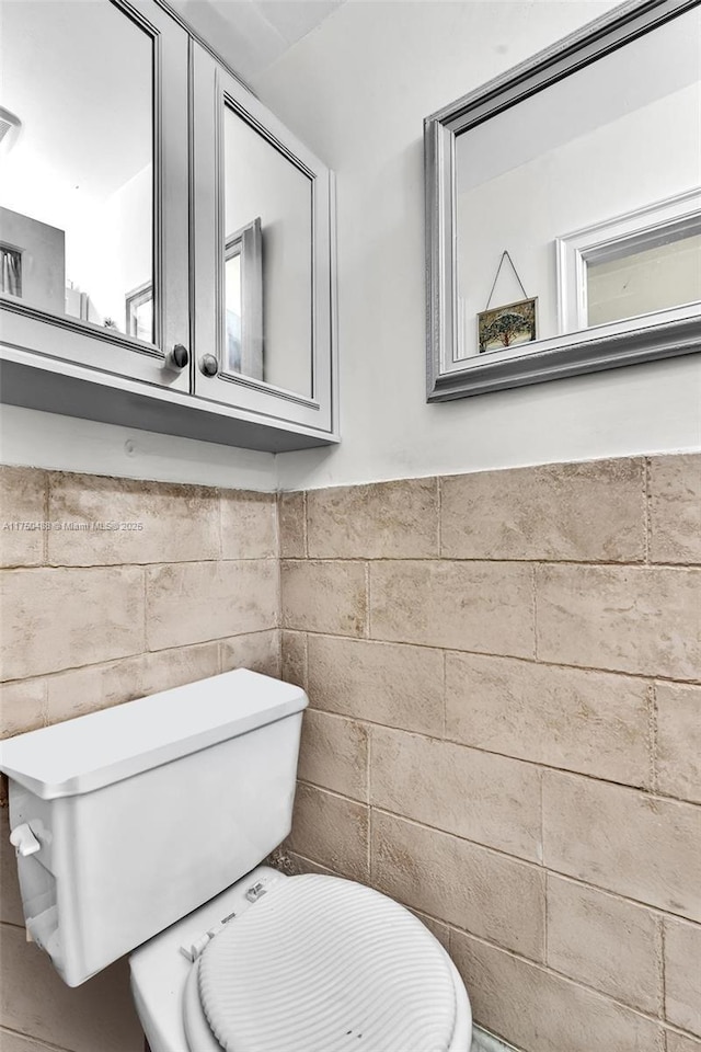 bathroom with wainscoting, toilet, and tile walls