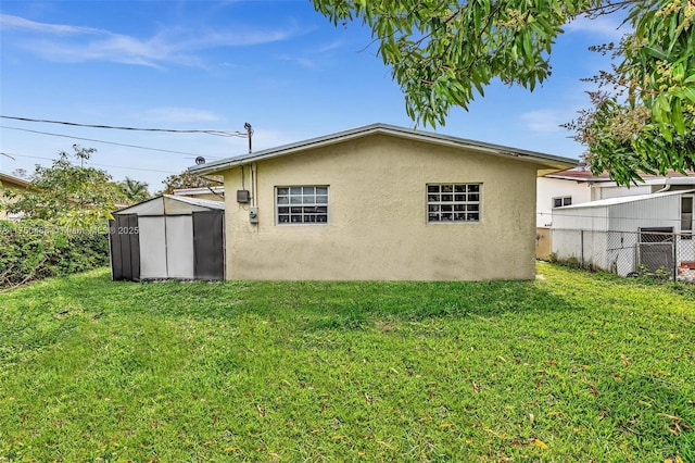 rear view of property with an outbuilding, a yard, a storage unit, stucco siding, and fence