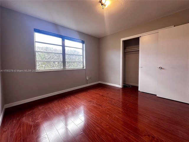 unfurnished bedroom with a closet, dark wood finished floors, and baseboards