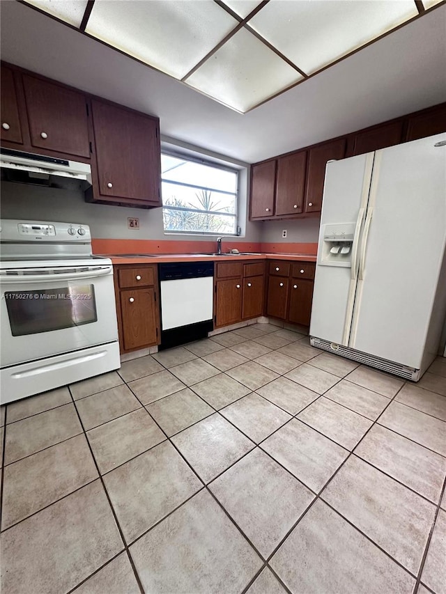 kitchen with white appliances, under cabinet range hood, light tile patterned floors, and a sink