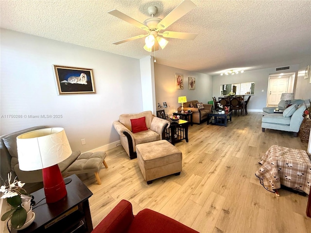 living room with a textured ceiling, light wood-type flooring, visible vents, and baseboards