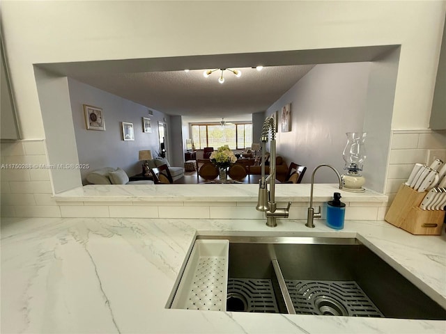 interior space featuring a sink, a textured ceiling, decorative backsplash, and light stone countertops