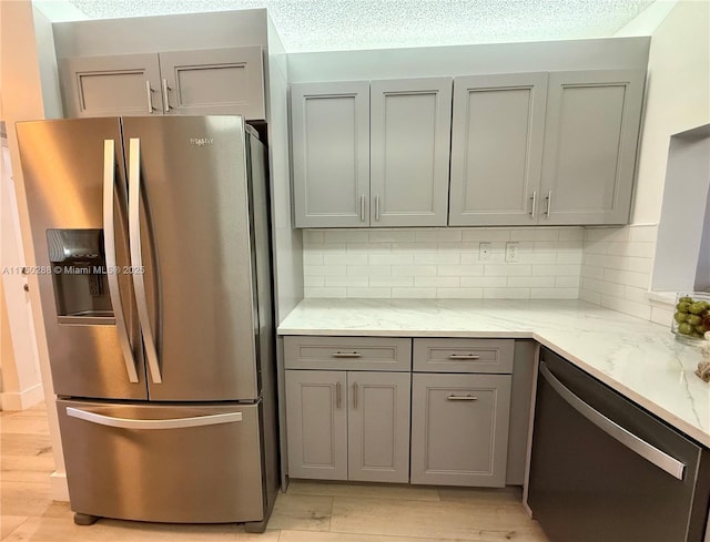 kitchen featuring stainless steel fridge, decorative backsplash, dishwashing machine, light stone counters, and gray cabinets