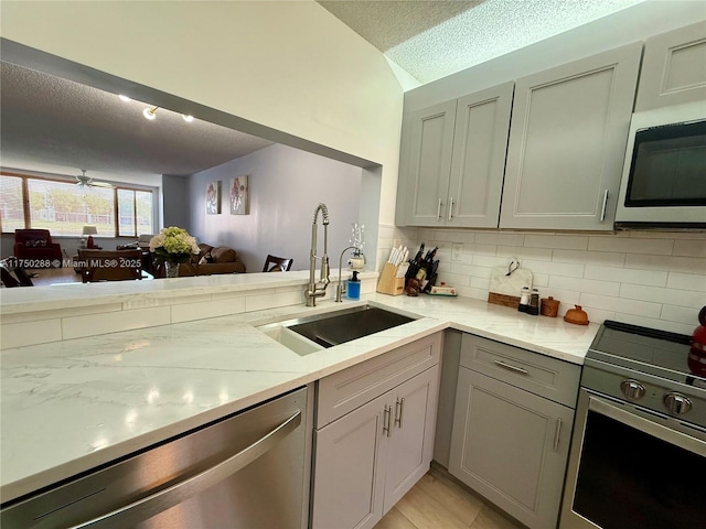 kitchen with tasteful backsplash, light stone counters, stainless steel appliances, a textured ceiling, and a sink