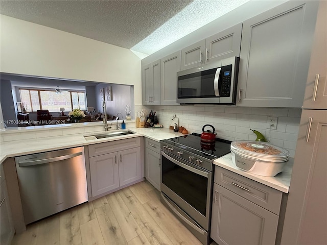 kitchen with stainless steel appliances, gray cabinets, light countertops, light wood-style flooring, and a sink