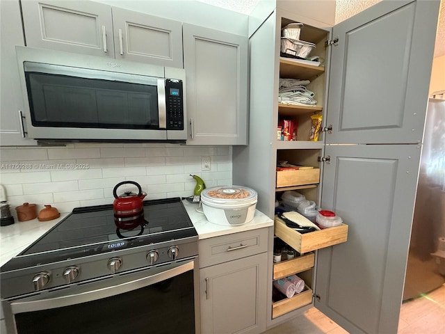 kitchen with appliances with stainless steel finishes, light countertops, decorative backsplash, and open shelves