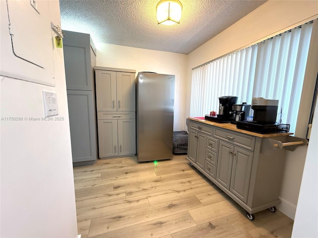 kitchen with dark countertops, gray cabinets, freestanding refrigerator, a textured ceiling, and light wood-type flooring