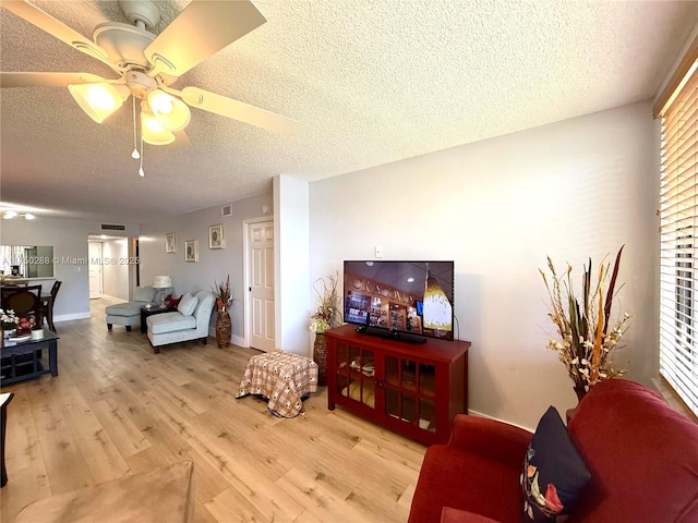 living area with light wood finished floors, ceiling fan, visible vents, and a textured ceiling