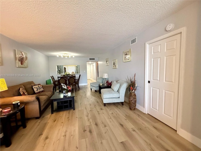 living area featuring light wood-type flooring, baseboards, visible vents, and a textured ceiling