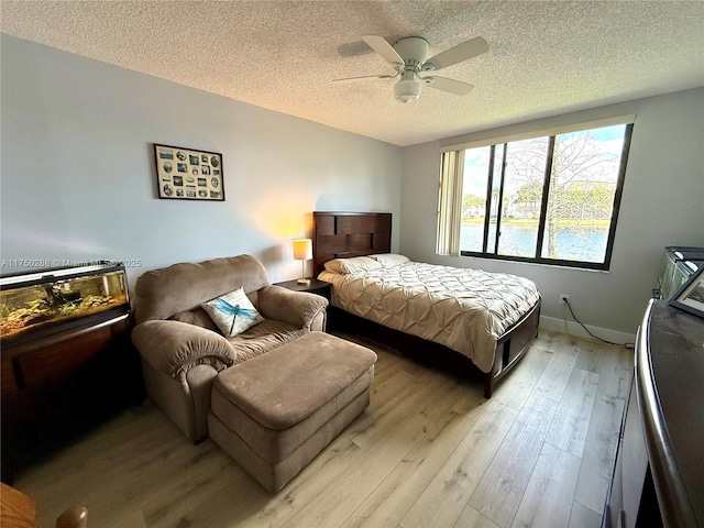 bedroom with a textured ceiling, light wood finished floors, a ceiling fan, and baseboards