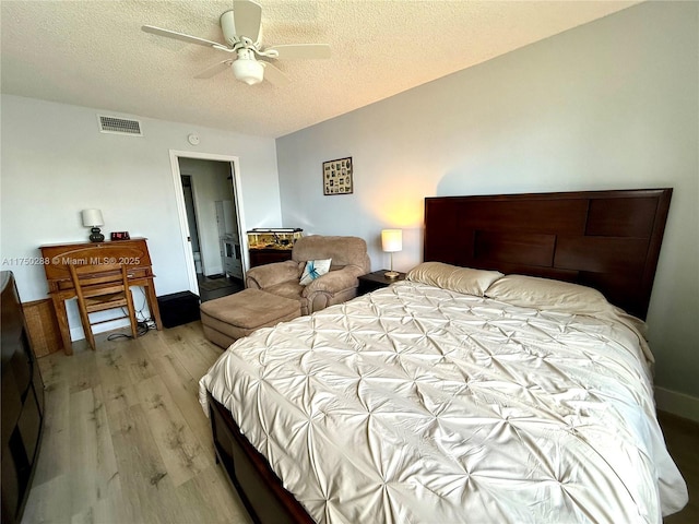 bedroom featuring light wood-style floors, a ceiling fan, visible vents, and a textured ceiling