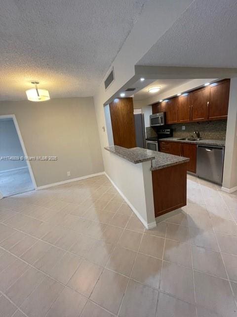 kitchen featuring visible vents, decorative backsplash, a peninsula, stainless steel appliances, and a sink