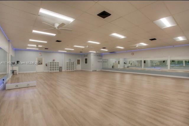 exercise room with a paneled ceiling, light wood finished floors, ceiling fan, and visible vents