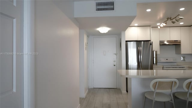 kitchen with white electric range oven, visible vents, white cabinets, freestanding refrigerator, and light countertops