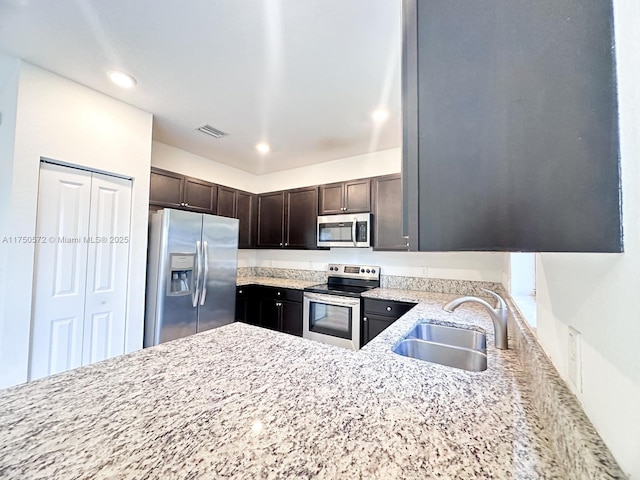 kitchen with dark brown cabinetry, visible vents, appliances with stainless steel finishes, light stone counters, and a sink