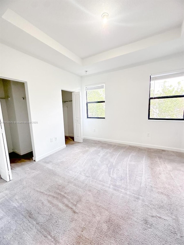 unfurnished bedroom featuring a tray ceiling, light colored carpet, and baseboards