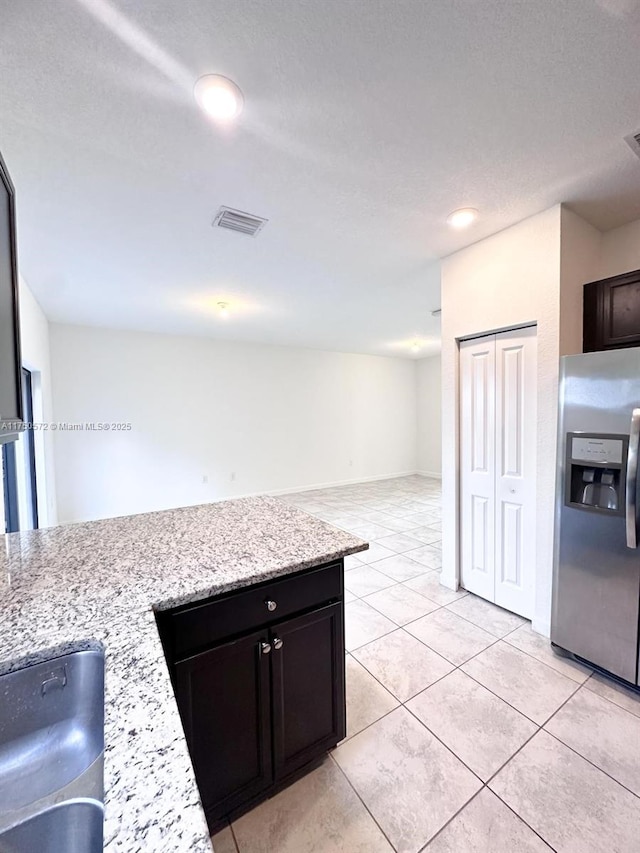 kitchen featuring light tile patterned flooring, dark brown cabinetry, visible vents, stainless steel refrigerator with ice dispenser, and light stone countertops