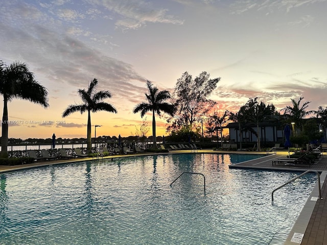 pool at dusk with a patio area, a community pool, and fence