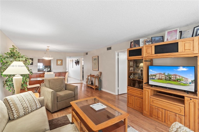 living area featuring a textured ceiling, light wood-type flooring, visible vents, and baseboards