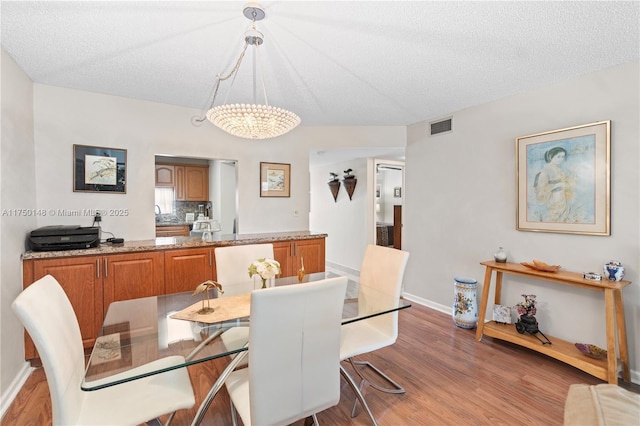 dining space with a textured ceiling, a chandelier, visible vents, baseboards, and light wood-style floors