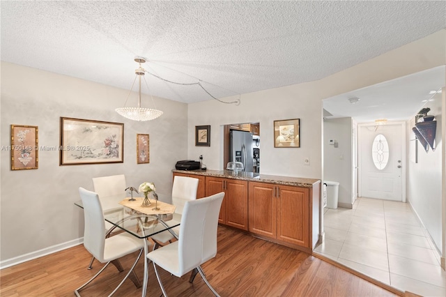 dining room featuring a textured ceiling, light wood-type flooring, and baseboards