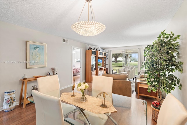 dining area featuring a textured ceiling, wood finished floors, visible vents, and baseboards