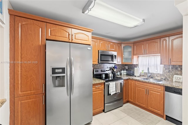 kitchen featuring light stone counters, tasteful backsplash, appliances with stainless steel finishes, glass insert cabinets, and a sink