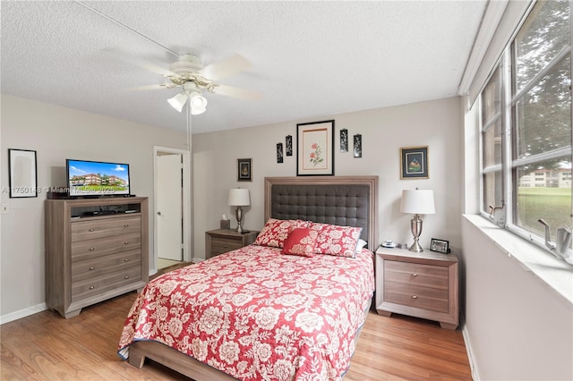 bedroom with a ceiling fan, baseboards, light wood-style flooring, and a textured ceiling