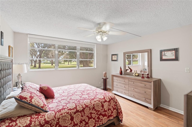 bedroom with light wood finished floors, ceiling fan, baseboards, and a textured ceiling