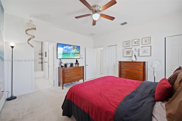 carpeted bedroom featuring connected bathroom, visible vents, multiple closets, and ceiling fan
