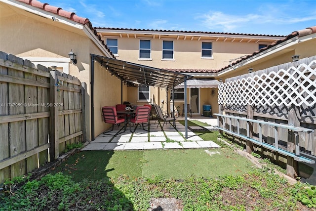rear view of property featuring a tiled roof, stucco siding, fence, and a patio