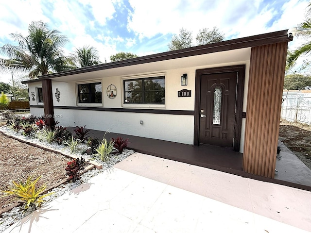 view of exterior entry with fence and stucco siding