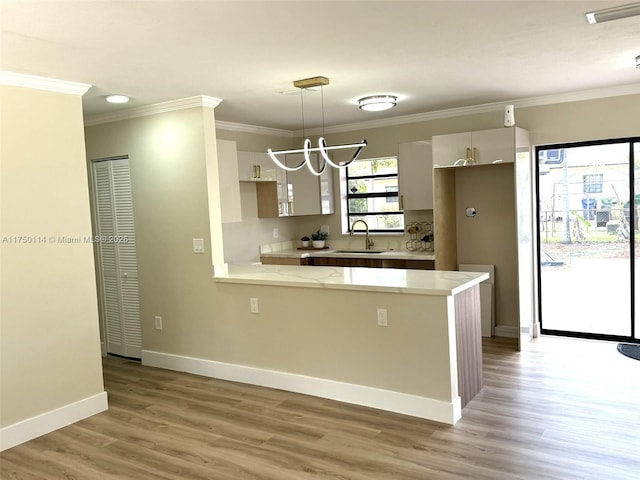 kitchen featuring a peninsula, light countertops, crown molding, pendant lighting, and a sink