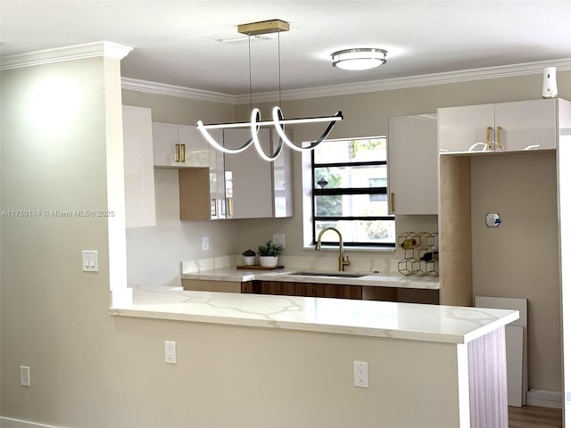 kitchen with white cabinets, light stone counters, ornamental molding, a peninsula, and a sink