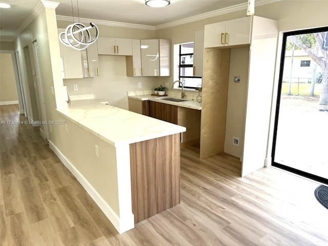 kitchen featuring white cabinets, hanging light fixtures, crown molding, light wood-style floors, and a sink