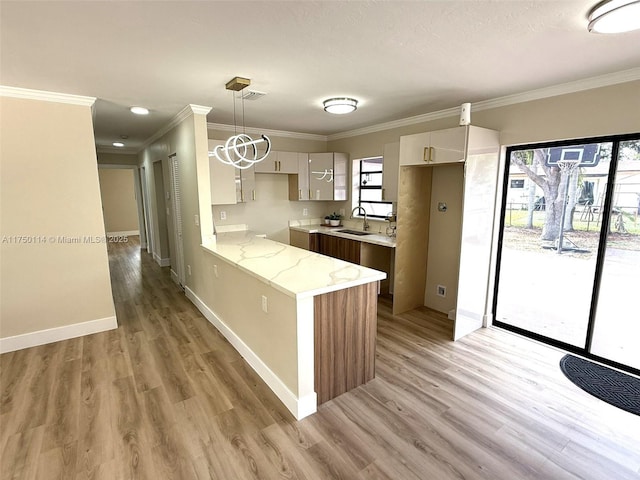 kitchen with a peninsula, a sink, light wood-style floors, decorative light fixtures, and crown molding