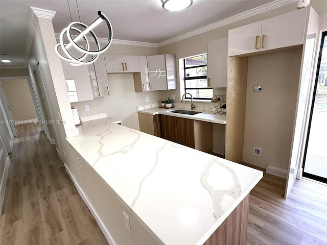 kitchen featuring light stone counters, white cabinetry, pendant lighting, and a sink