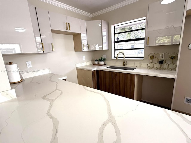 kitchen with light stone counters, tasteful backsplash, ornamental molding, white cabinets, and a sink